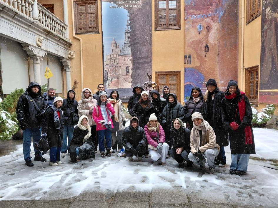 Un grupo de personas sonrientes posando en un paisaje nevado frente a un mural colorido.