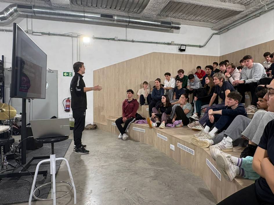 Un orador se dirige a un grupo de jóvenes sentados en gradas en un espacio moderno.