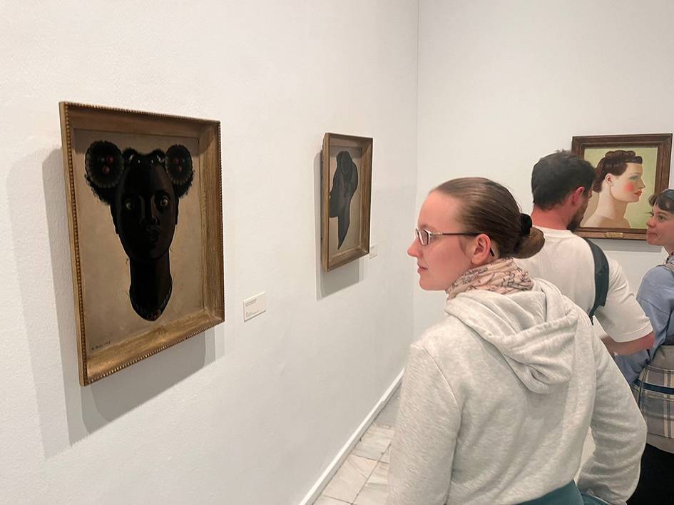 Una persona observa obras de arte en una galería, destacando cuadros en las paredes con retratos llamativos.