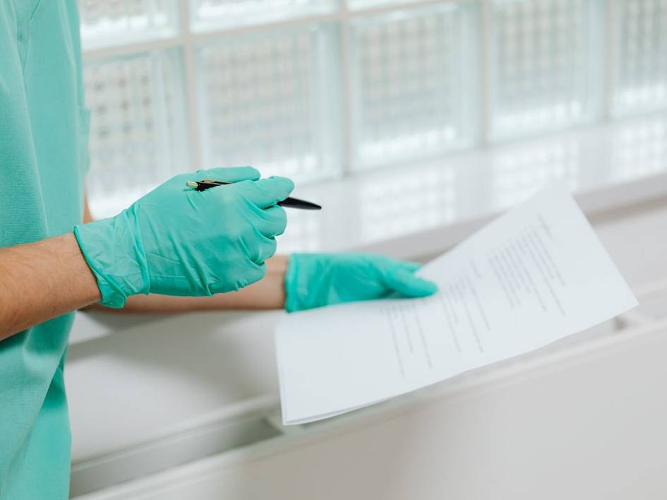 Una persona con guantes de látex sostiene un documento mientras escribe.