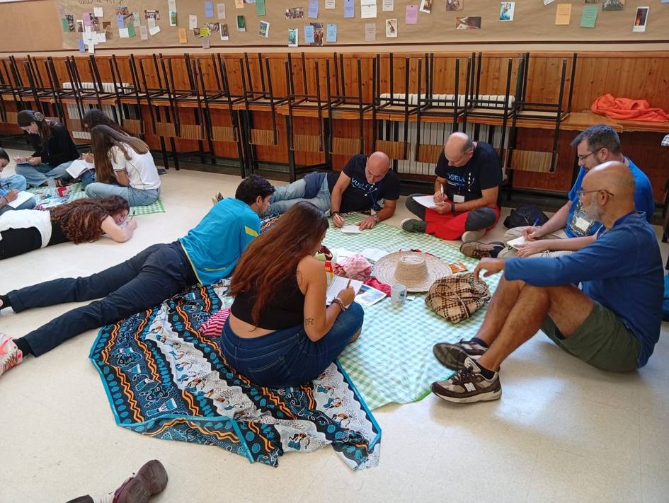 Un grupo de personas sentadas en el suelo, organizando actividades en un ambiente de convivencia.