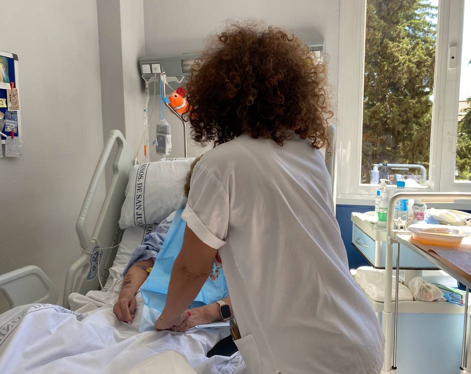 A healthcare worker is checking on a patient in a hospital bed.
