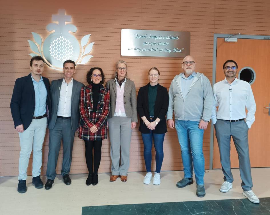 Grupo de siete personas sonriendo en un vestíbulo frente a un logo corporativo y un letrero inspiracional.