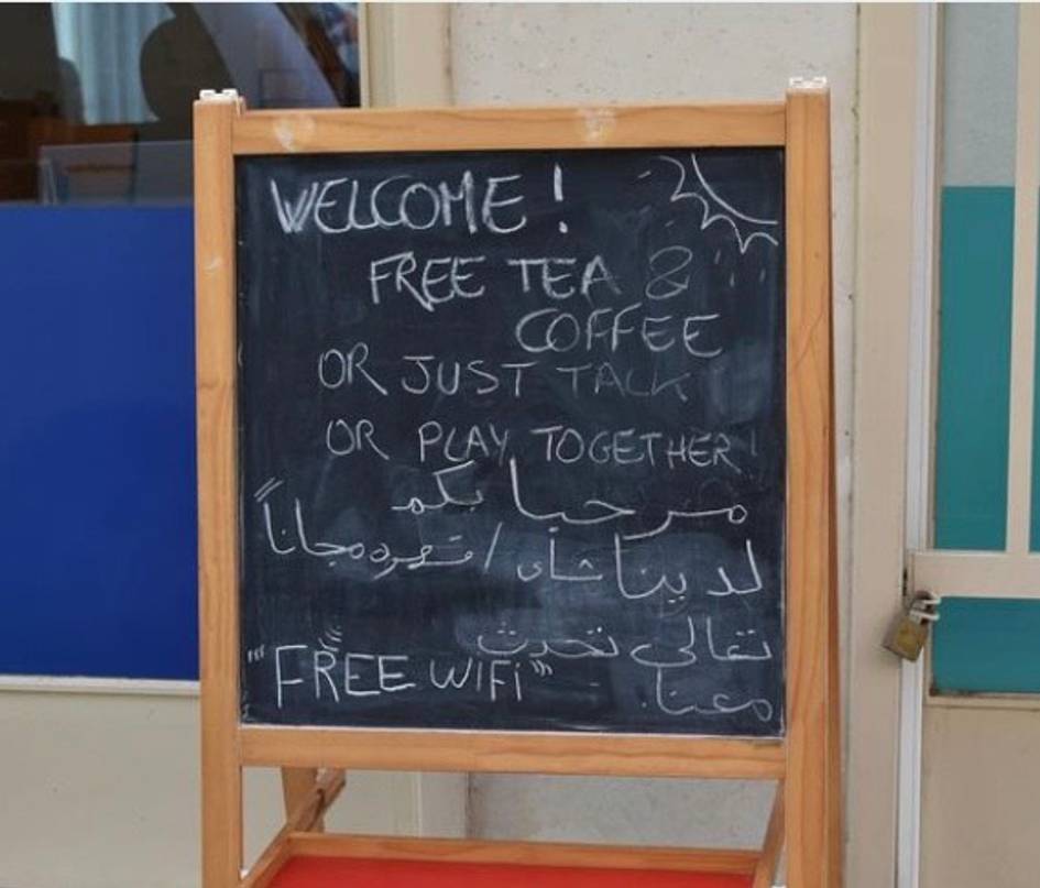 A chalkboard with a welcoming message offering free tea, coffee, and wifi, including text in multiple languages.