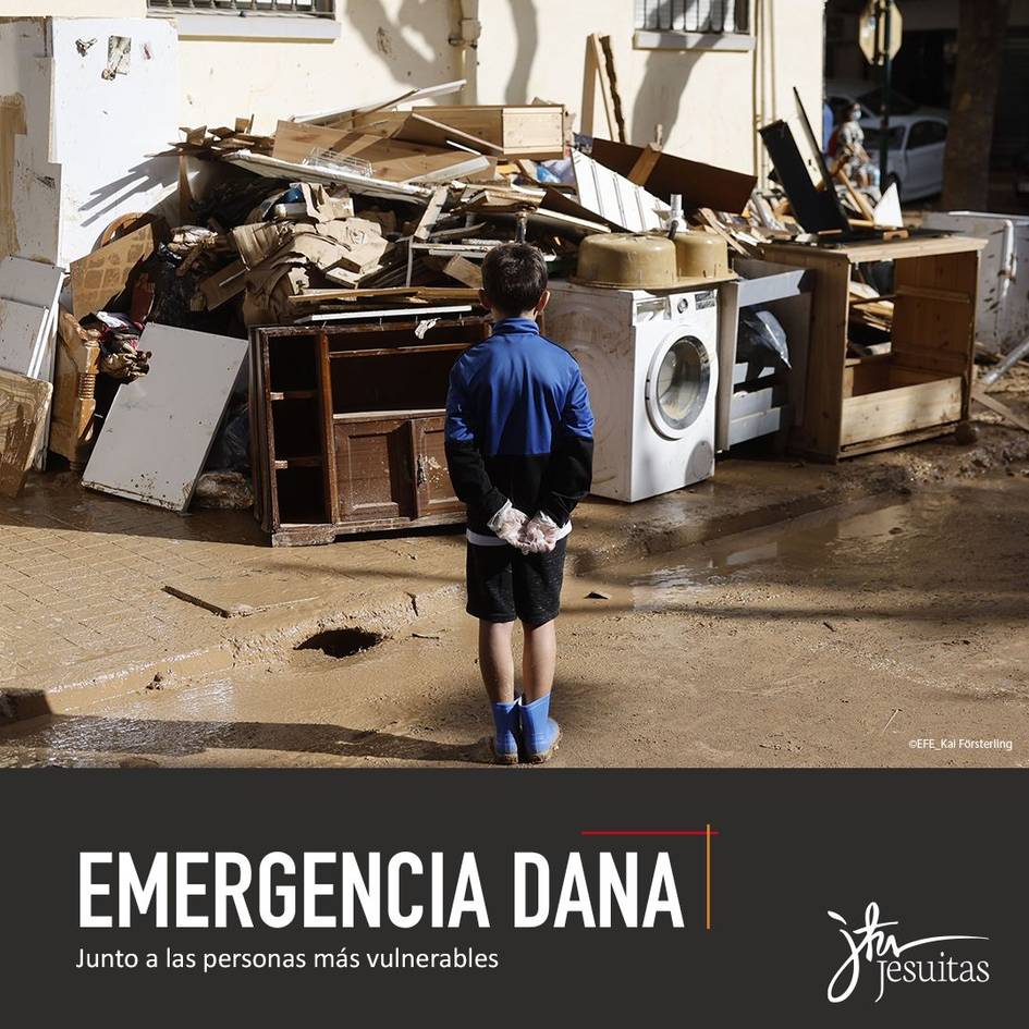 A young person stands amidst a pile of debris and damaged household items on a muddy street, observing the devastation.