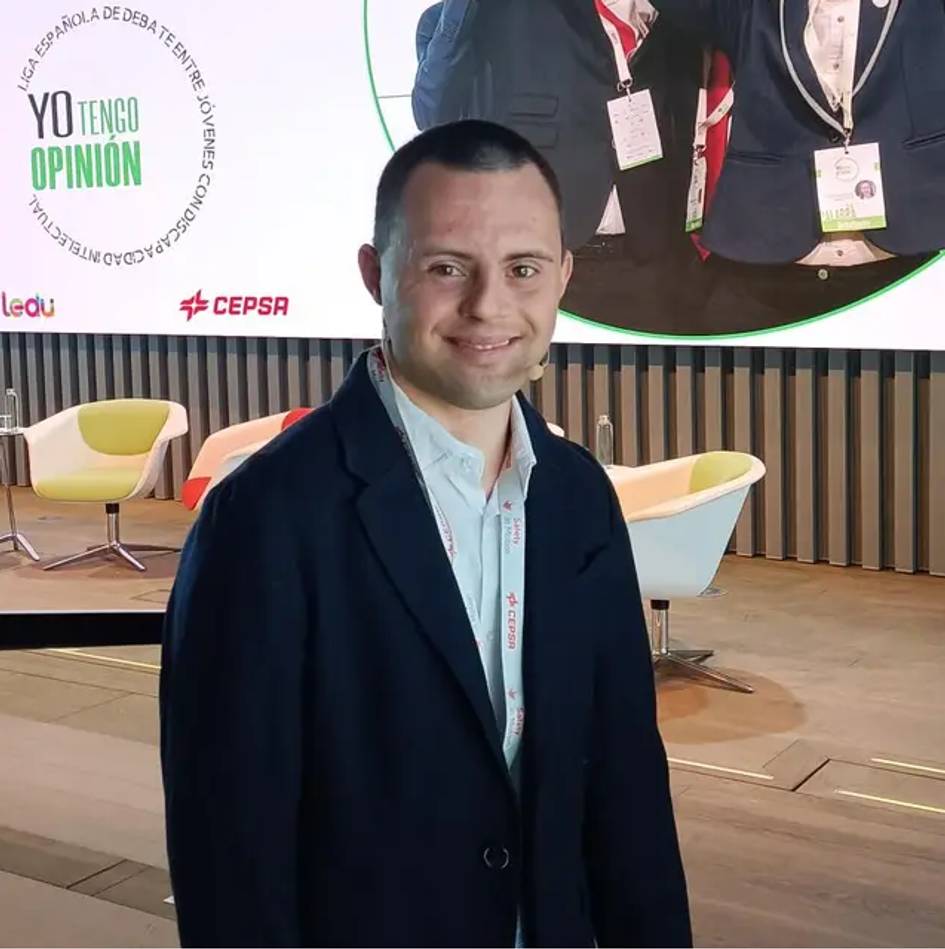 A man smiling at a conference event with banners in the background.