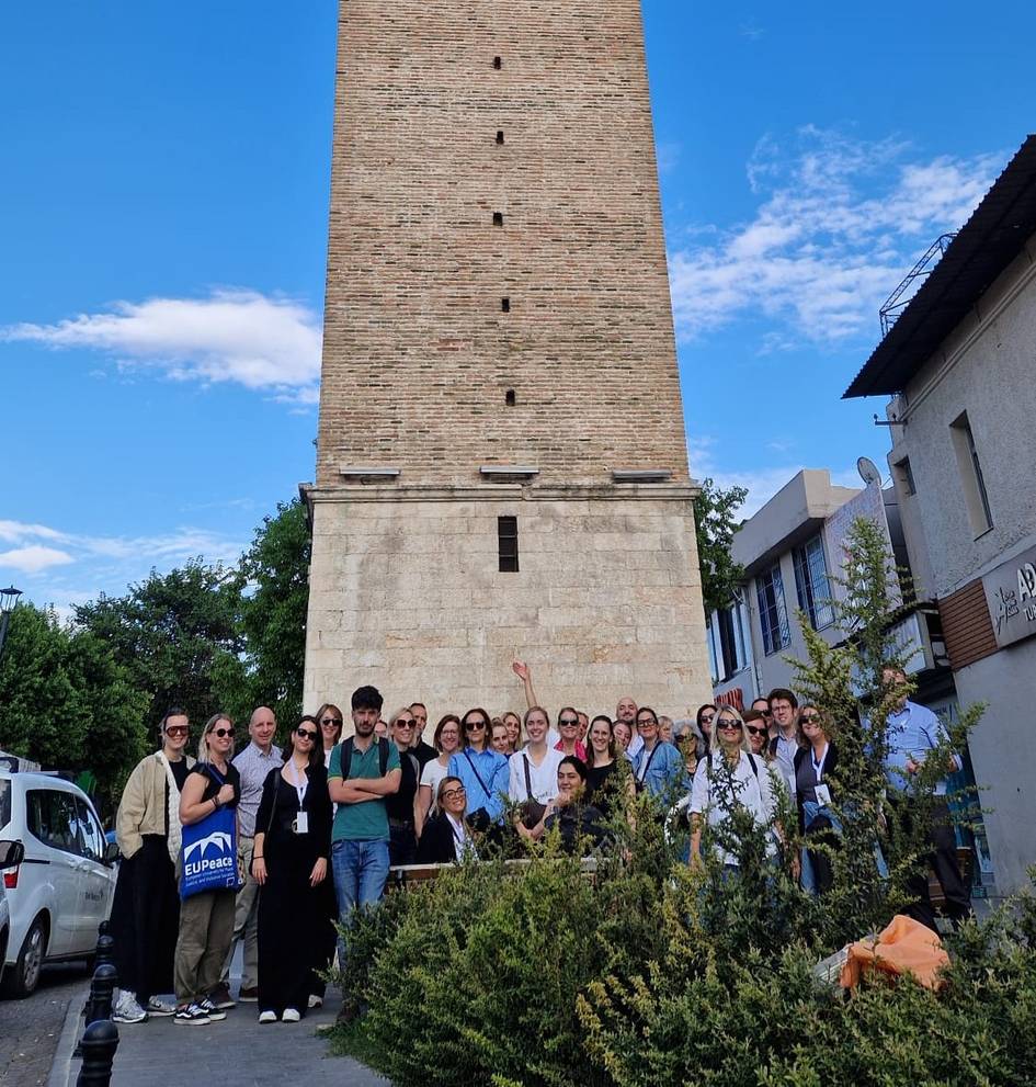 Un grupo de personas posando frente a una torre de piedra bajo un cielo azul.