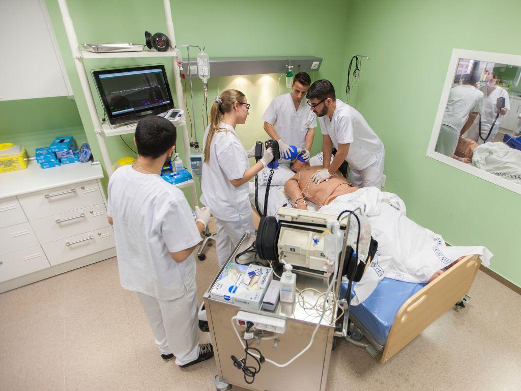 Medical professionals in scrubs practicing emergency procedures on a simulation mannequin in a hospital training room.