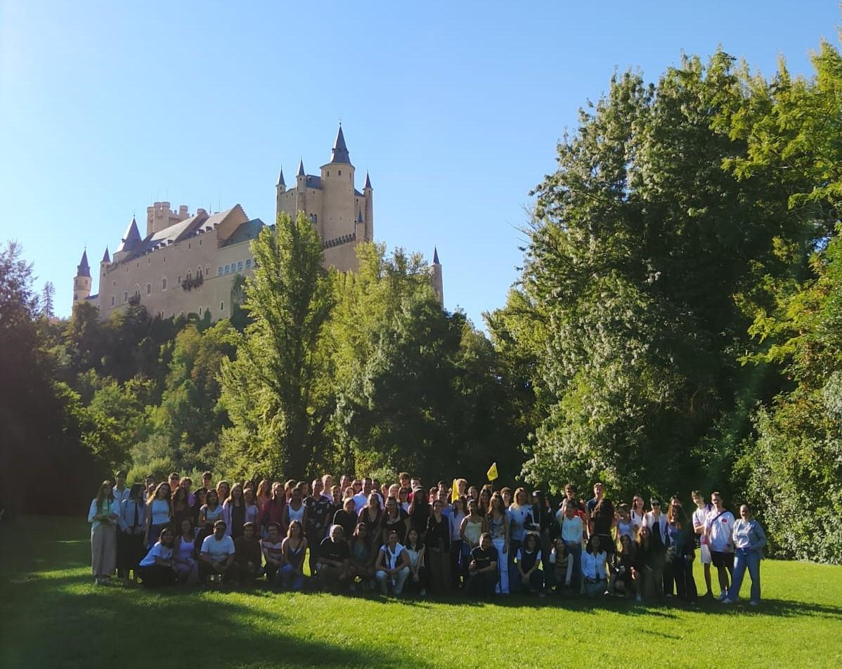 Un gran grupo de personas posando frente a un castillo rodeado de árboles en un día soleado.