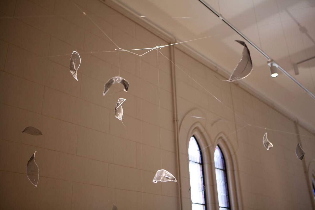 La imagen muestra una instalación artística con hojas de vidrio suspendidas en un espacio interior.