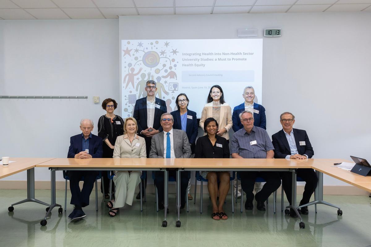 Un grupo de personas de pie y sentadas en una mesa, posando para una foto frente a una presentación sobre equidad en salud.