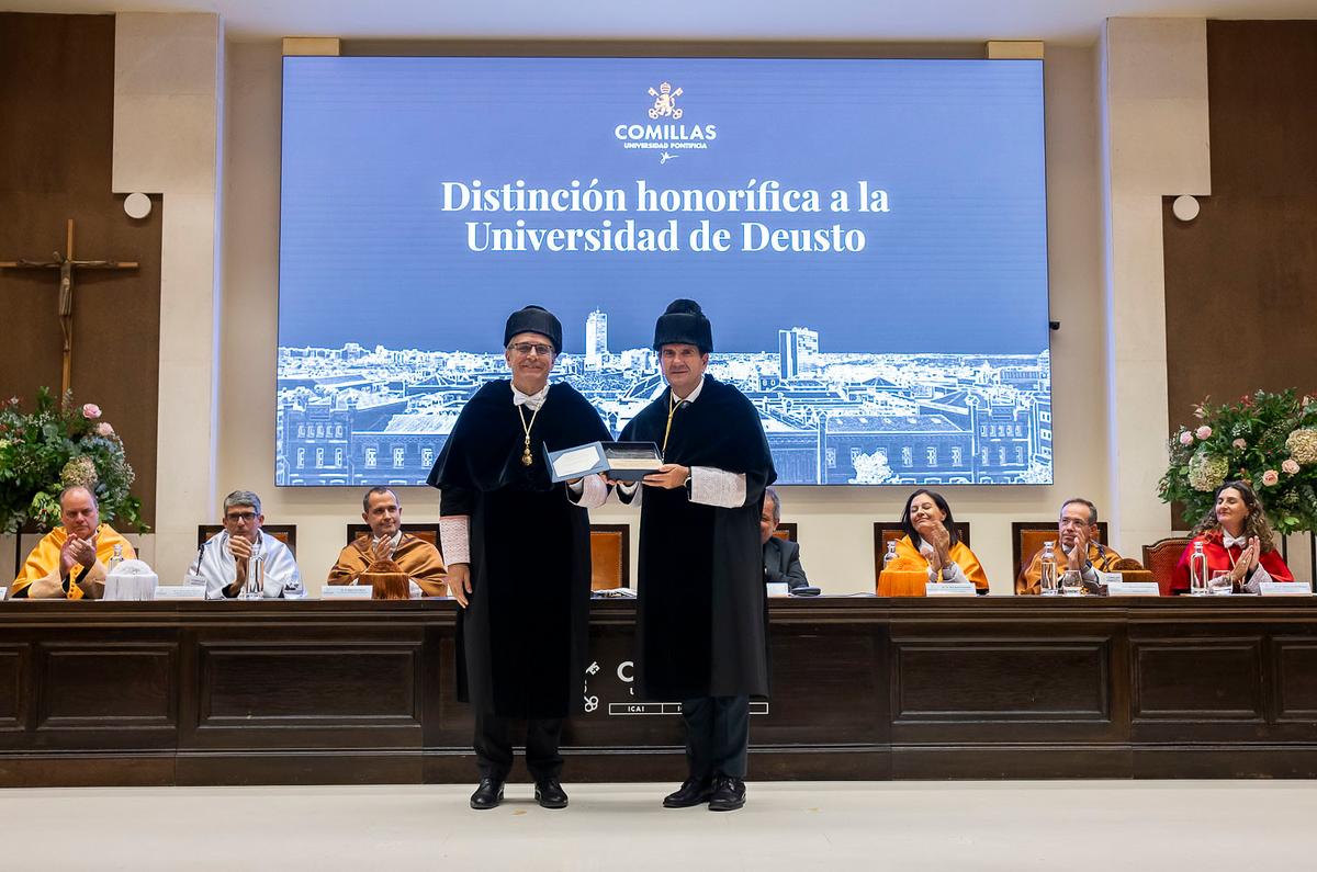 La imagen muestra una ceremonia de entrega de una distinción honorífica a la Universidad de Deusto en un evento formal.