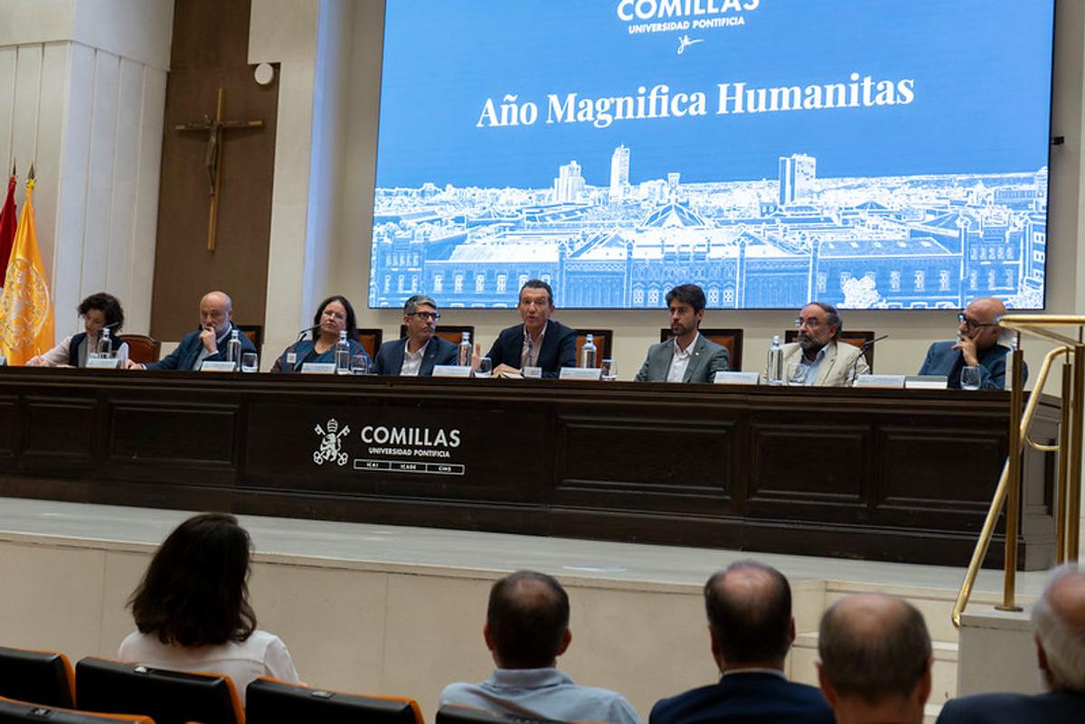 Un panel de discusión en la Universidad Pontificia Comillas con varios ponentes y una pantalla que anuncia el Año Magnífica Humanitas.