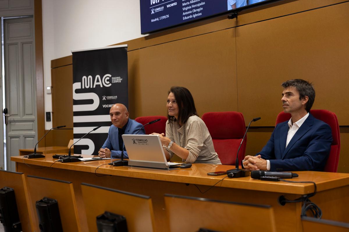 Una mesa de conferencias con tres ponentes en un auditorio.