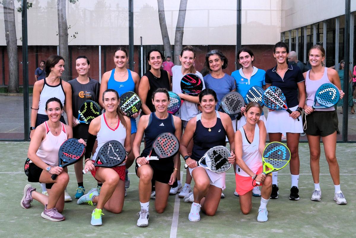 Un grupo de mujeres posando en una cancha de pádel con palas en la mano.