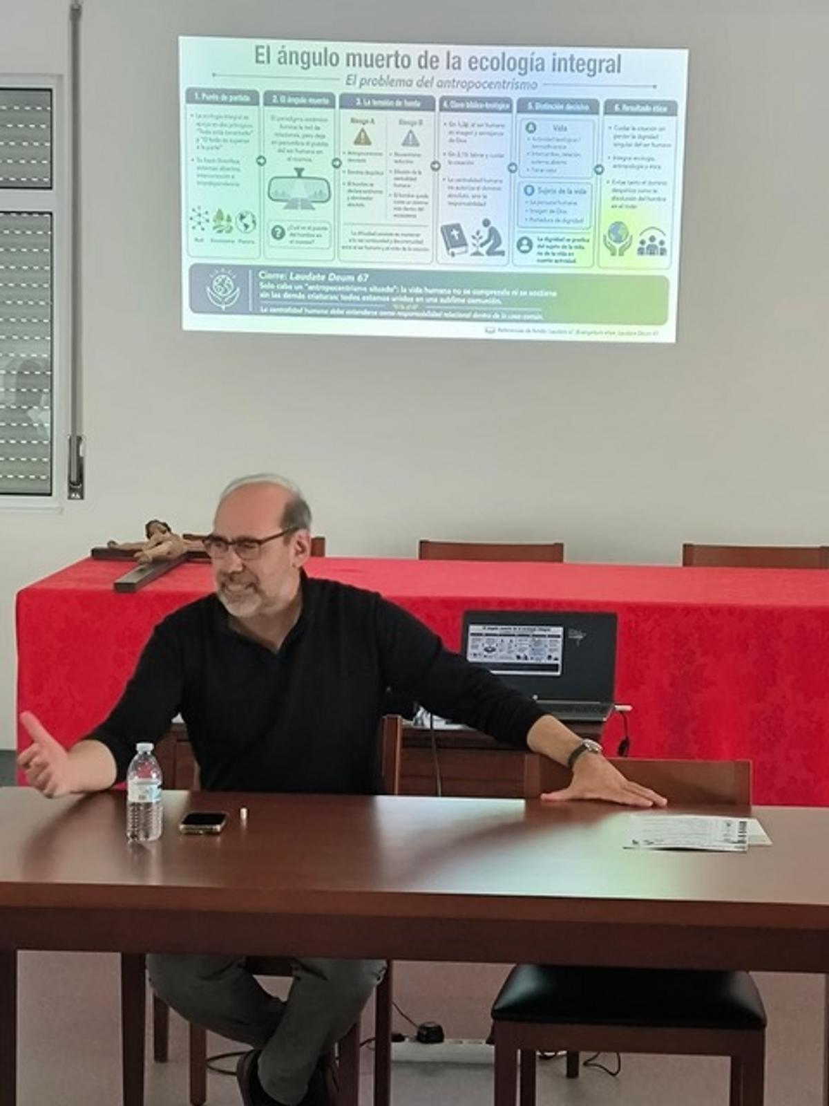 Un hombre sentado en una mesa frente a una presentación sobre ecología integral.