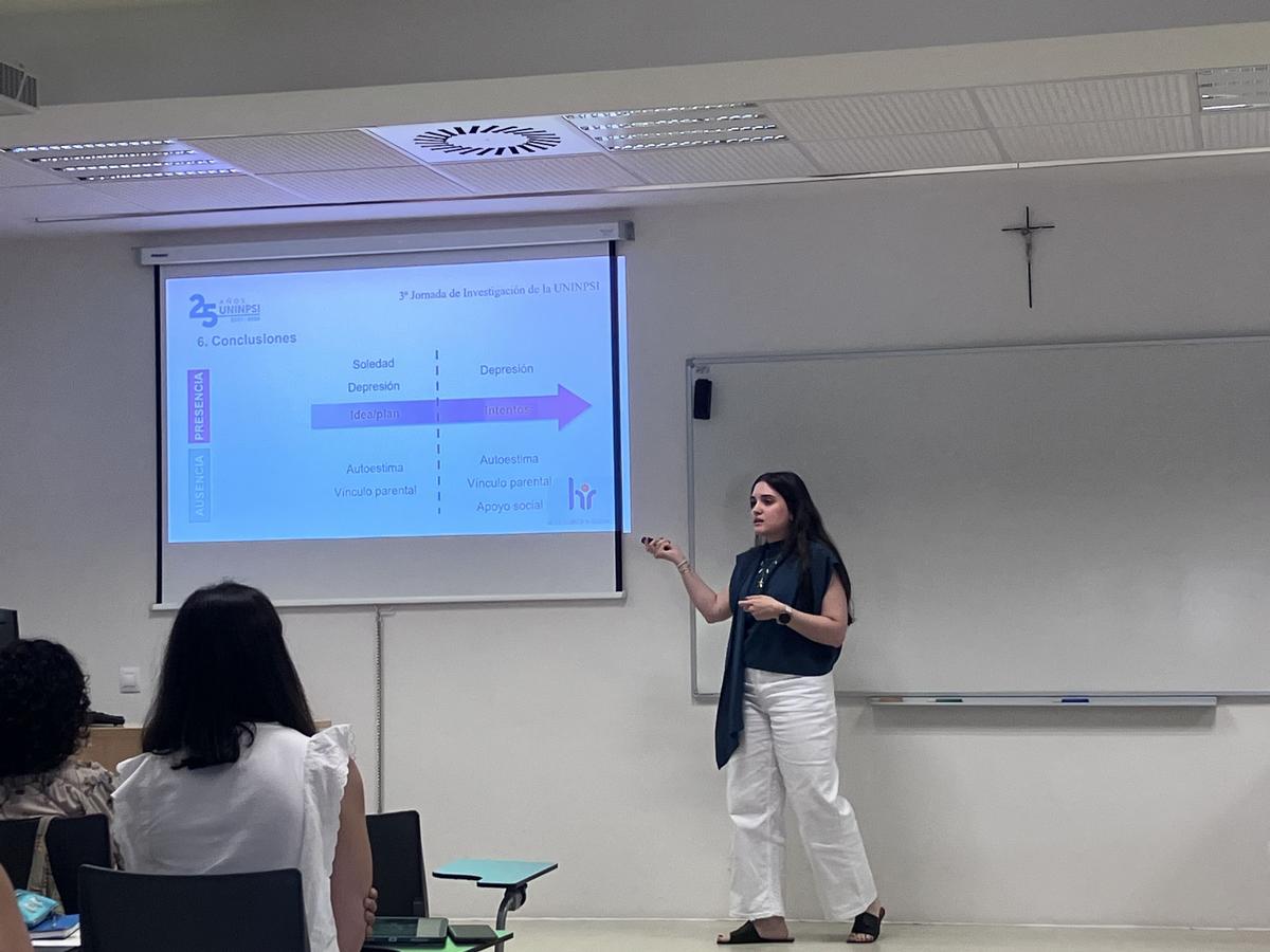 Una presentadora expone un tema frente a un grupo de personas en un aula.