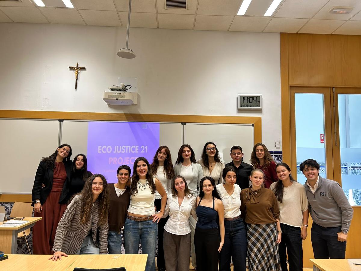 Grupo de estudiantes posando juntos en un aula con un proyecto relacionado con la justicia ecológica en el fondo.