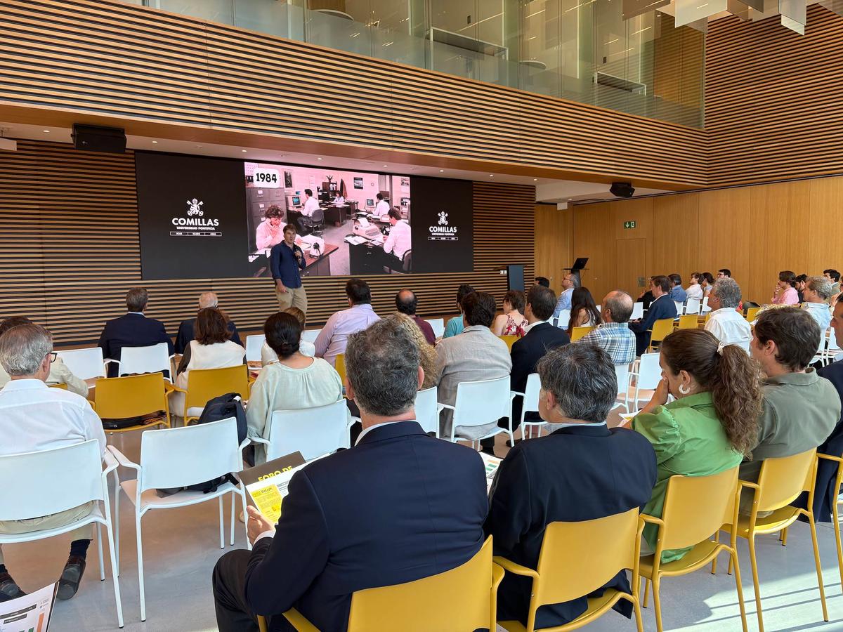 Una reunión celebrada en un auditorio moderno con un orador frente a una pantalla grande y una audiencia atenta.