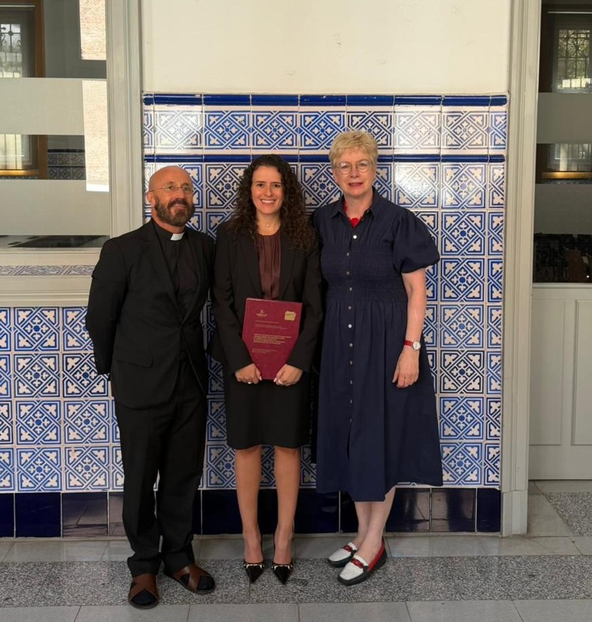 La imagen muestra a tres personas posando frente a un fondo de azulejos, celebrando un logro académico.