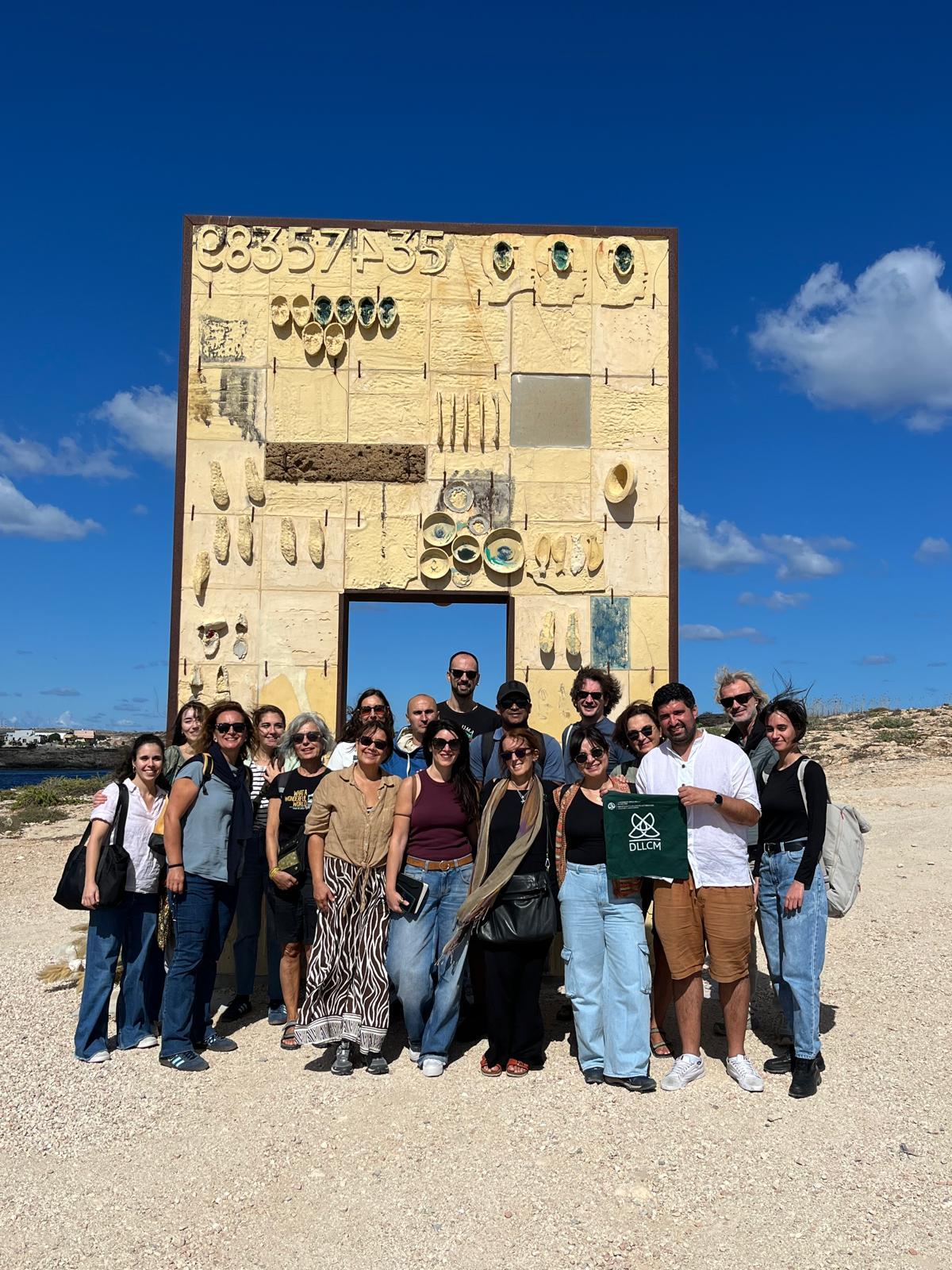 Un grupo de personas posando frente a una gran estructura artística en un paisaje despejado.
