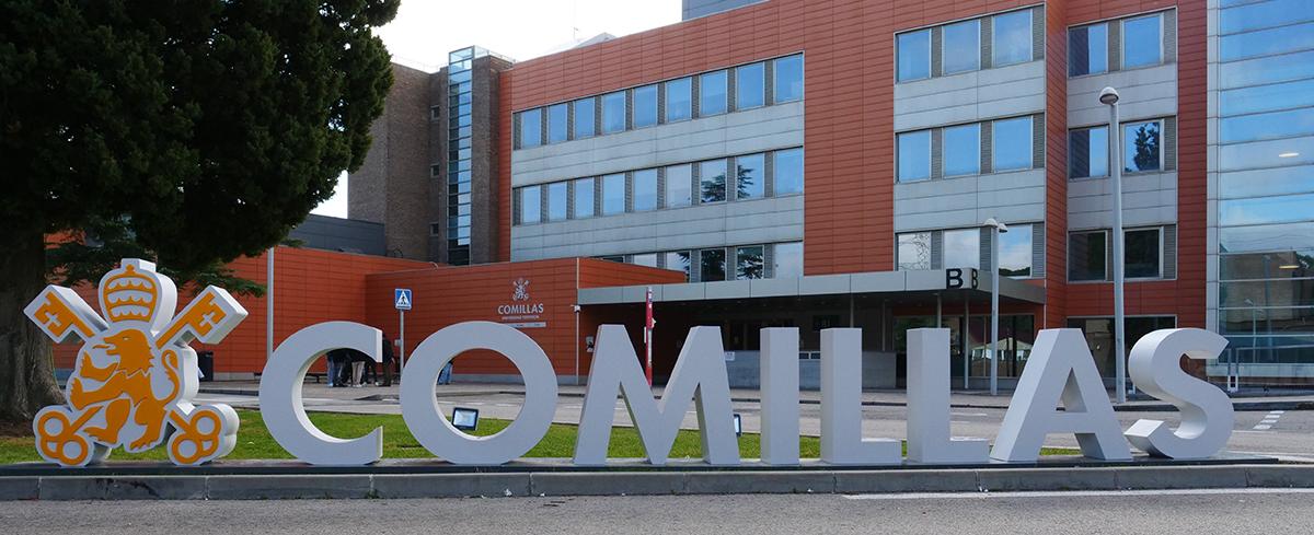 La imagen muestra la entrada a la Universidad Pontificia Comillas en un edificio moderno.