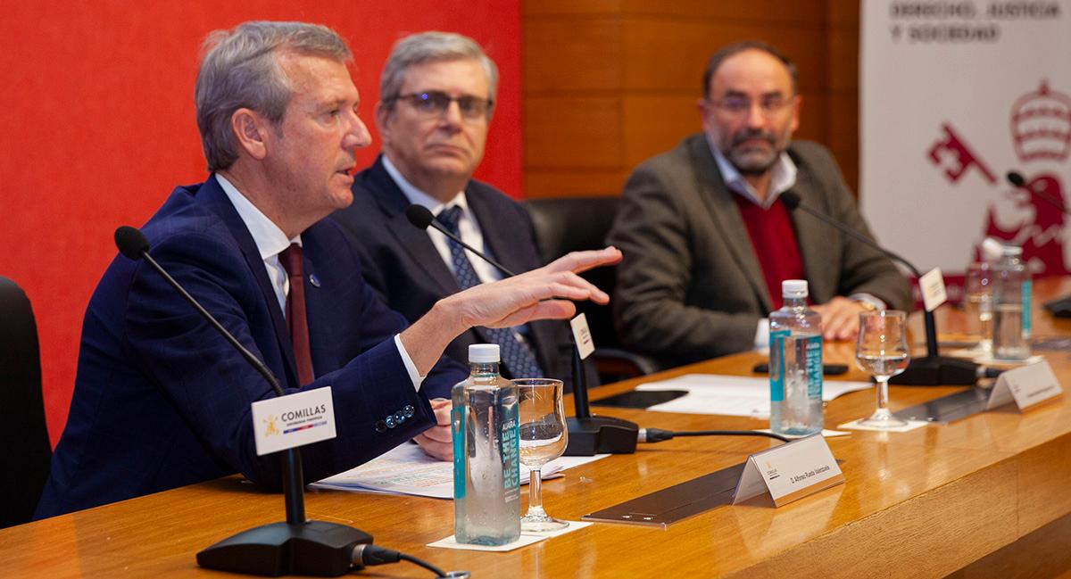 A man gestures while speaking at a conference panel alongside other participants.