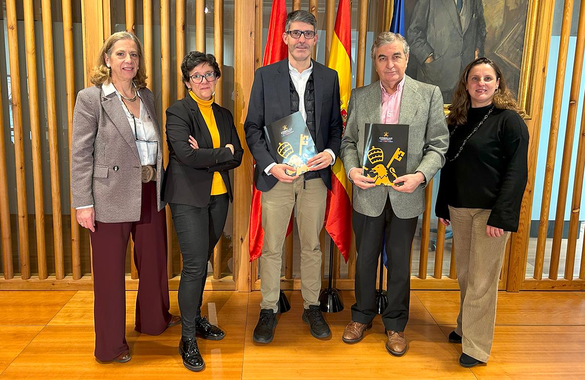 Un grupo de cinco personas posan frente a un fondo con banderas y paredes de madera, sosteniendo documentos en las manos.