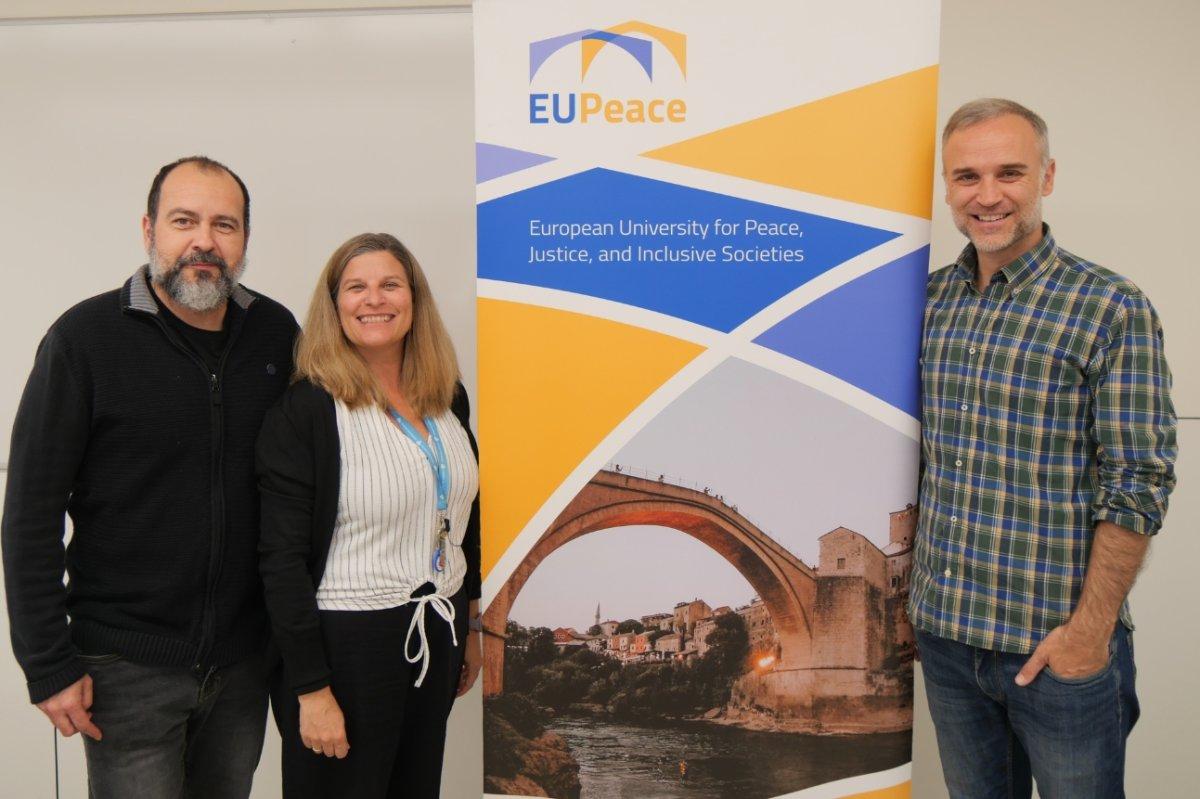Tres personas posan junto a un banner de la Universidad Europea de la Paz.