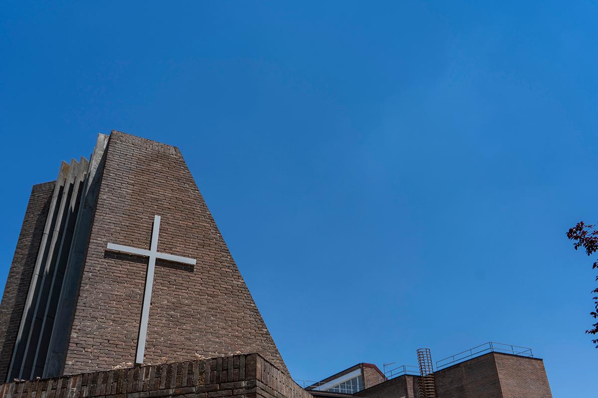 Una iglesia moderna con una cruz visible en su fachada y un cielo azul despejado de fondo.