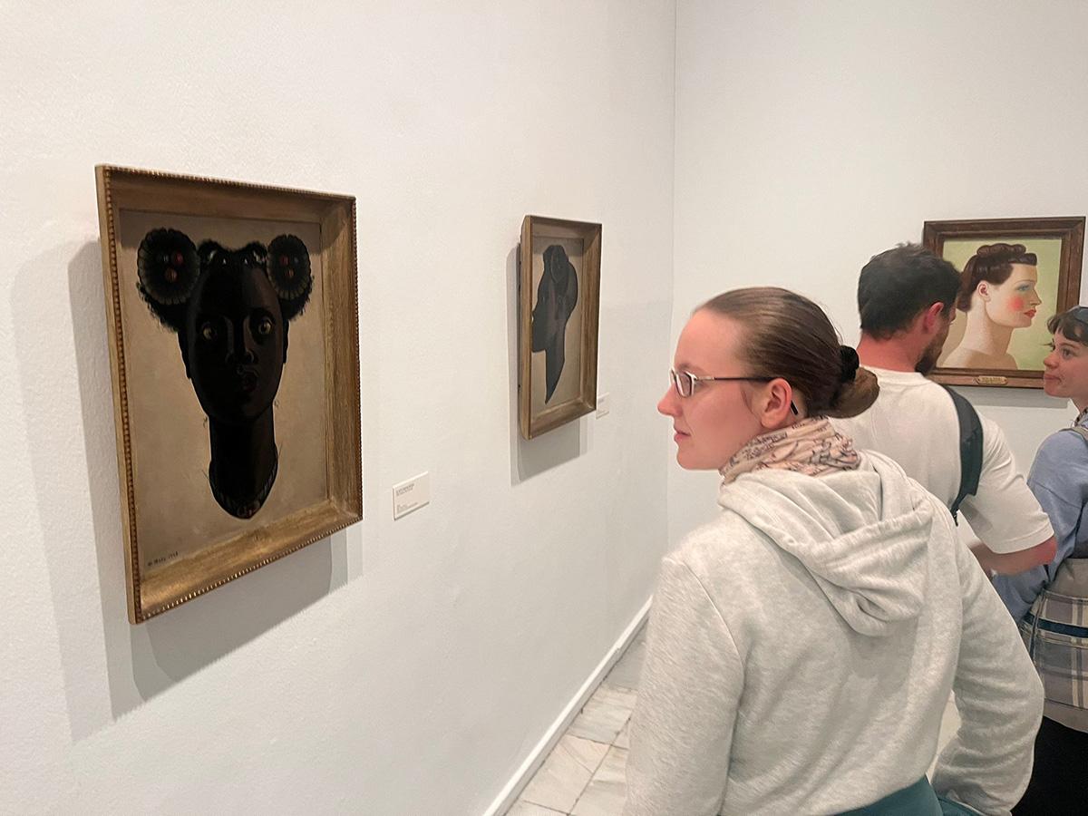 Una persona observa obras de arte en una galería, destacando cuadros en las paredes con retratos llamativos.