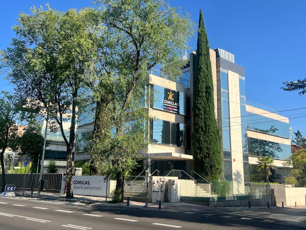 Edificio moderno rodeado de árboles y con un letrero que dice 'COMILLAS'.