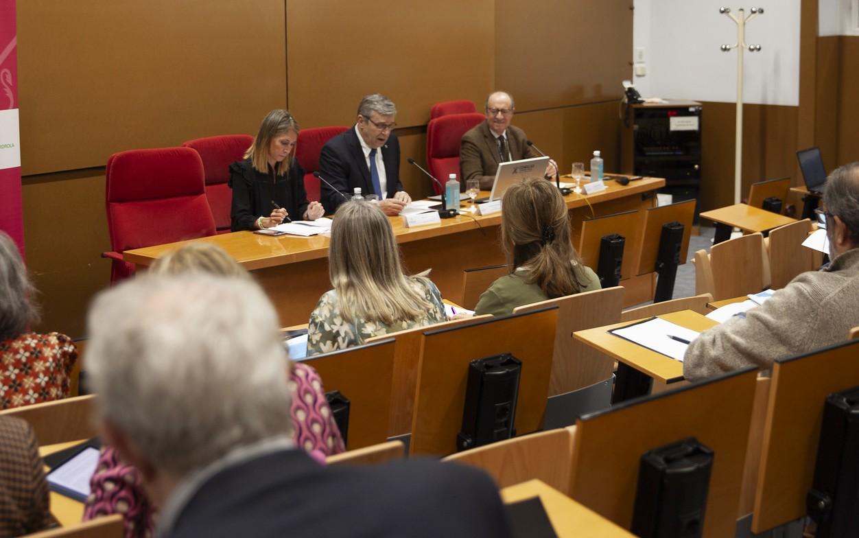 A professional meeting or conference is taking place in a modern hall with participants seated facing a panel of speakers.