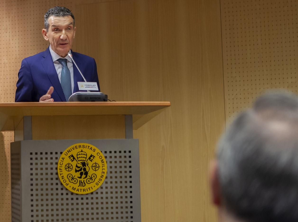 Un hombre en traje azul se encuentra dando una conferencia frente a un público parcialmente visible.