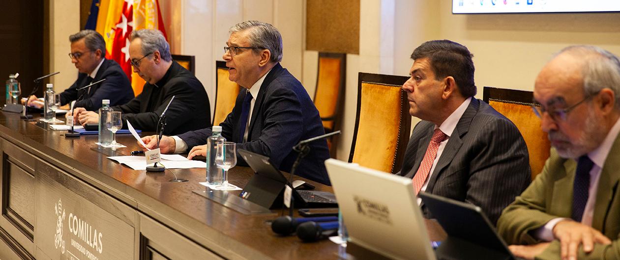 A group of men seated at a long table during a formal meeting or conference, with microphones and laptops in front of them.