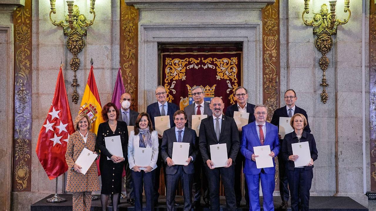 A group of people holding certificates inside an ornate hall with flags in the background.