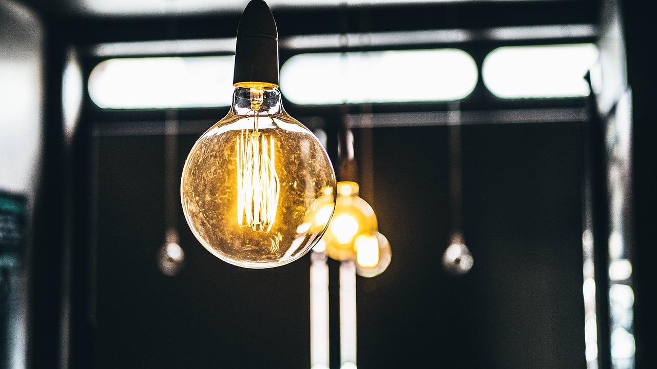 A close-up view of an illuminated filament light bulb against a blurred background.