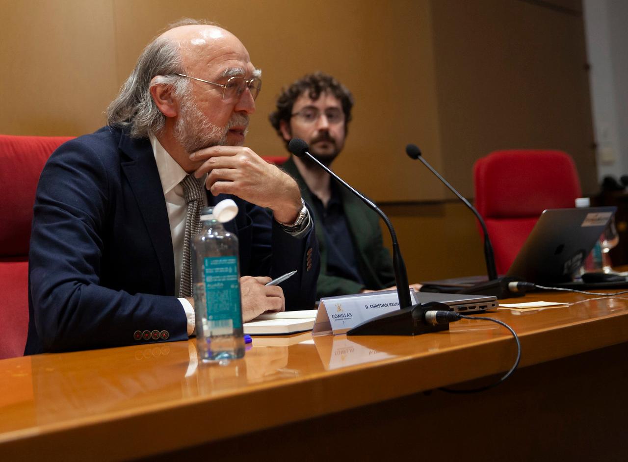 Dos hombres sentados en una mesa durante una conferencia o presentación.