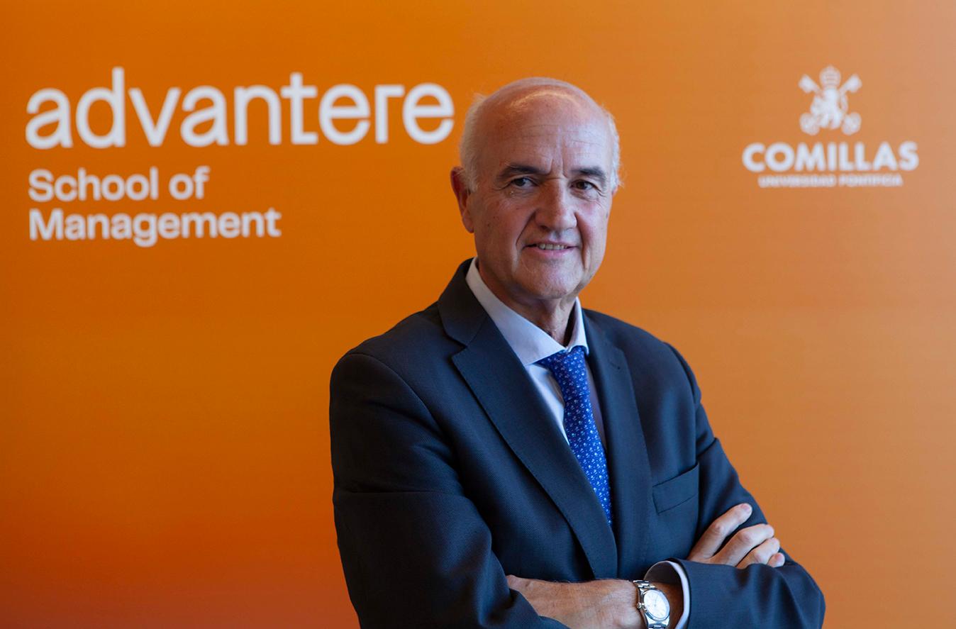 An older man in a suit stands confidently with his arms crossed in front of a sign that says 'advantere School of Management Comillas'.