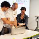 Three people, two men and a woman, are engaging in a cooking class, collaborating while preparing dough in a metal tray.