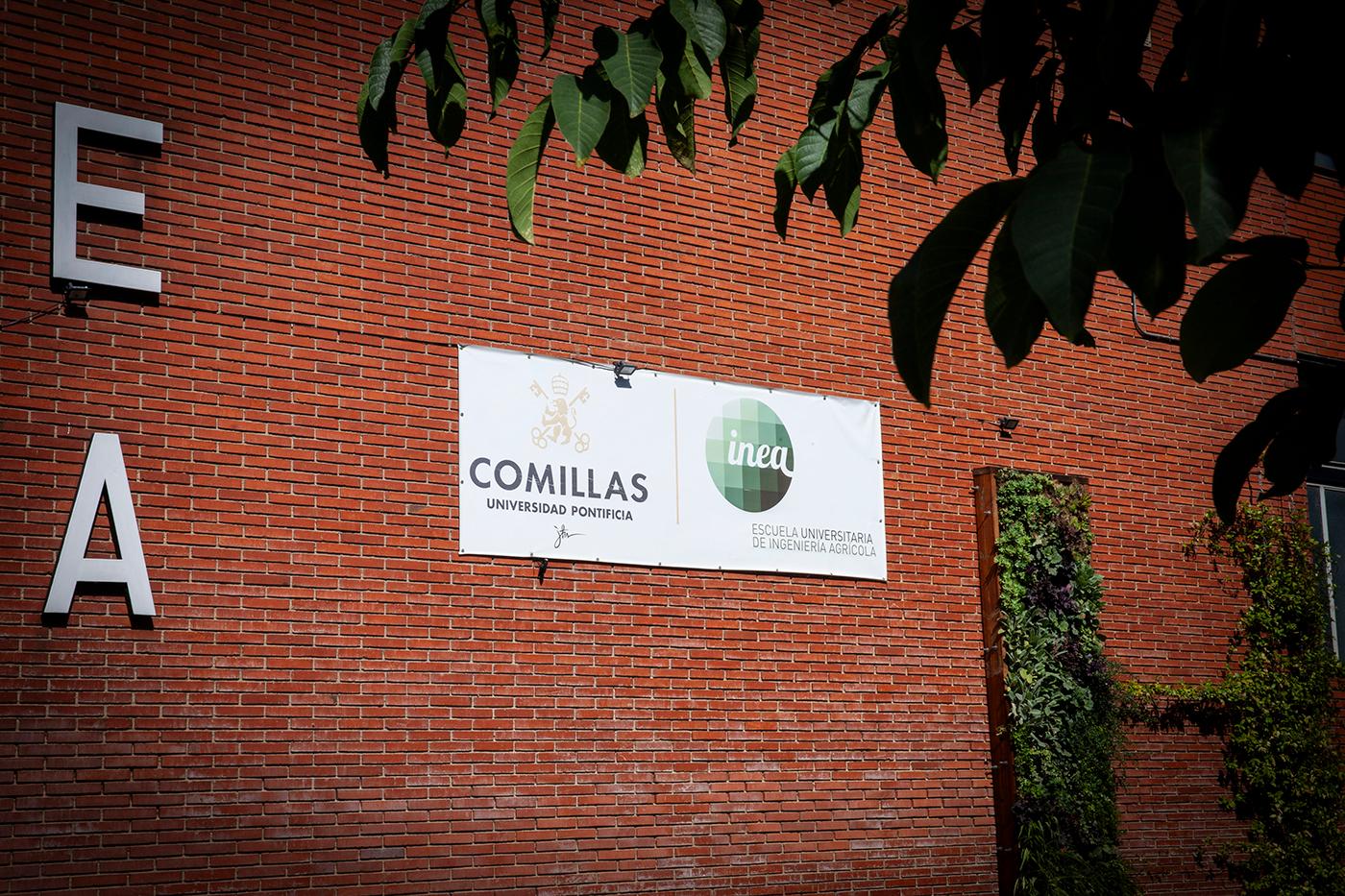 La imagen muestra un cartel de la Universidad Pontificia Comillas con el logotipo de INEA en una pared de ladrillo.