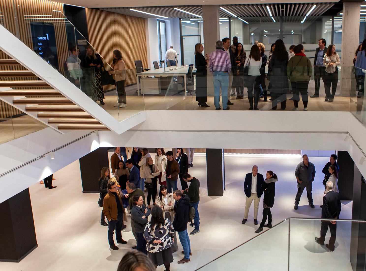 People gathering in a modern indoor space with a staircase and reception desk.