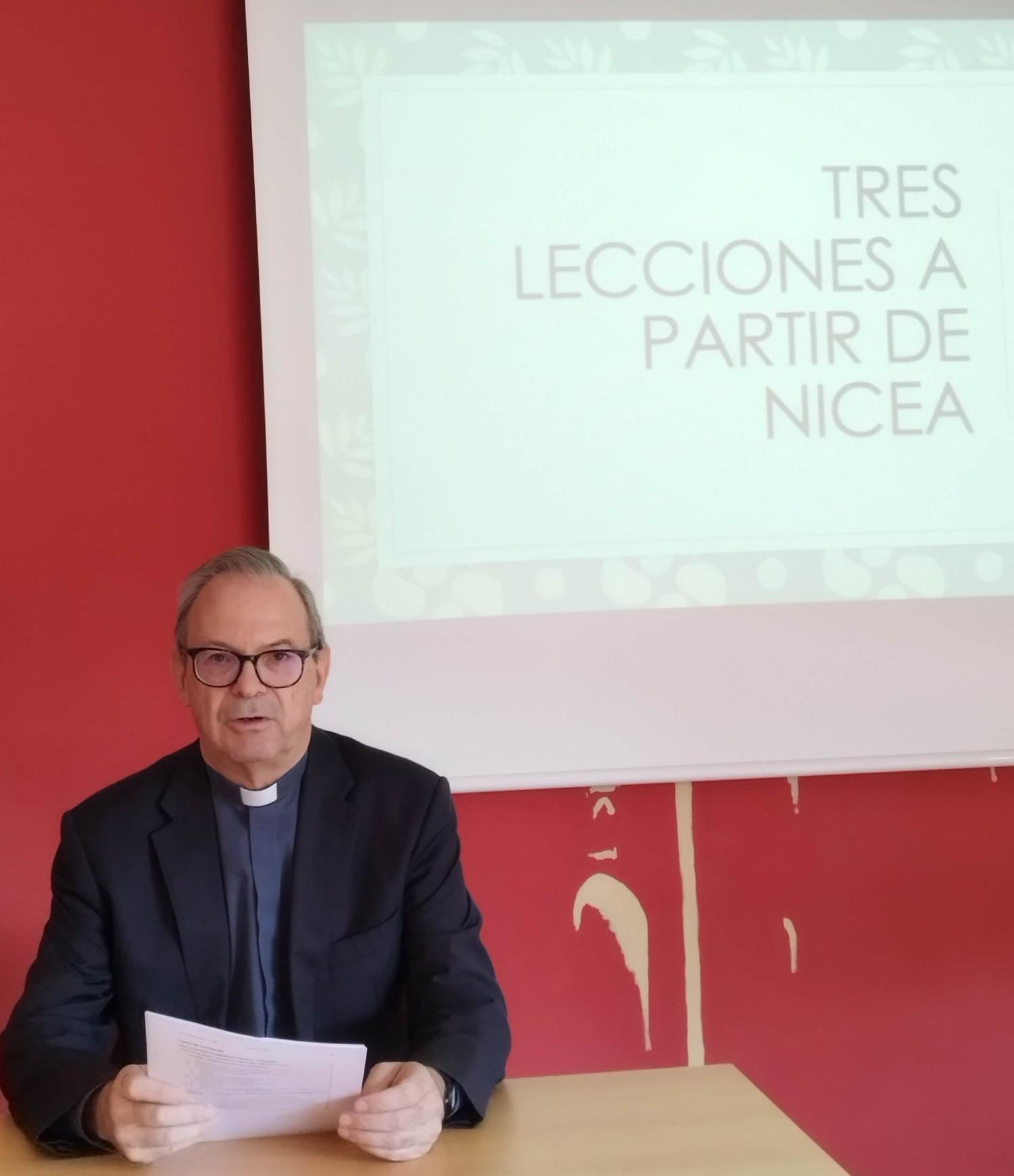 Una persona con vestimenta formal se encuentra en una mesa frente a una presentación sobre las lecciones de Nicea.