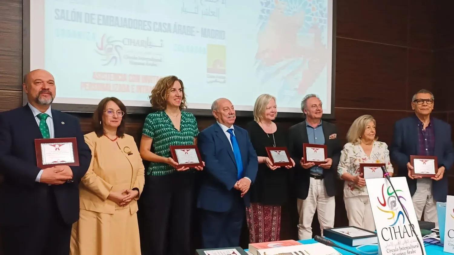 Group of eight people standing on a stage holding awards, with a banner in the background.