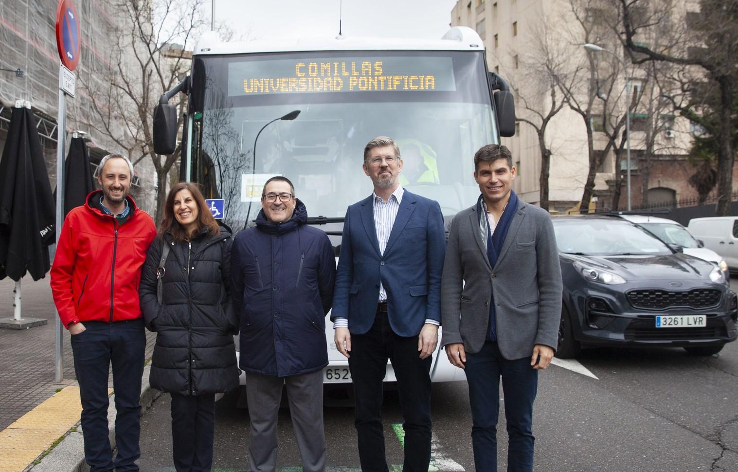 Un grupo de cinco personas se fotografía frente a un autobús con destino a la Universidad Pontificia Comillas.