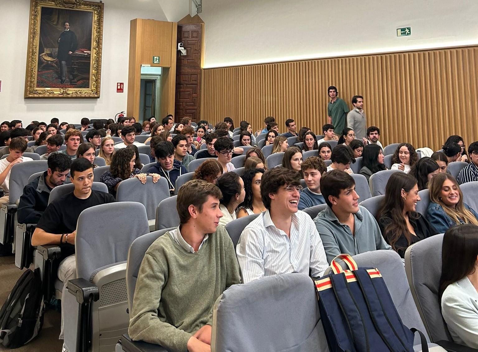 A group of students sitting in a lecture hall, some smiling and looking around.