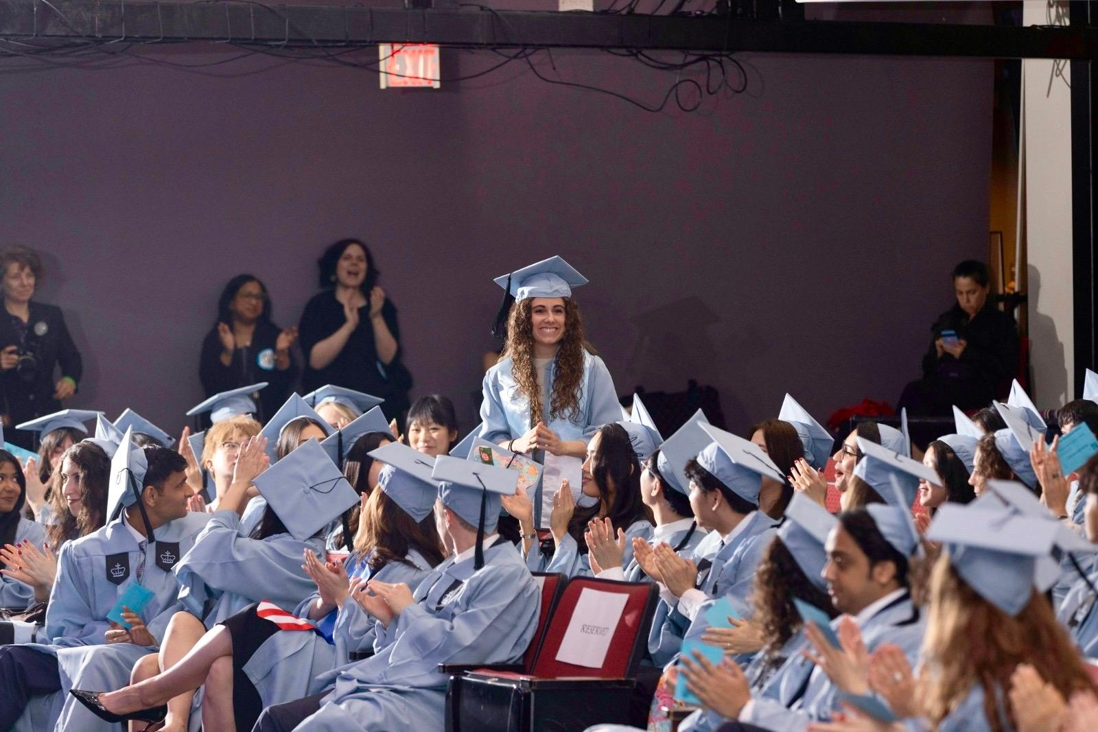 Una estudiante recibe aplausos durante una ceremonia de graduación con otros graduados a su alrededor.