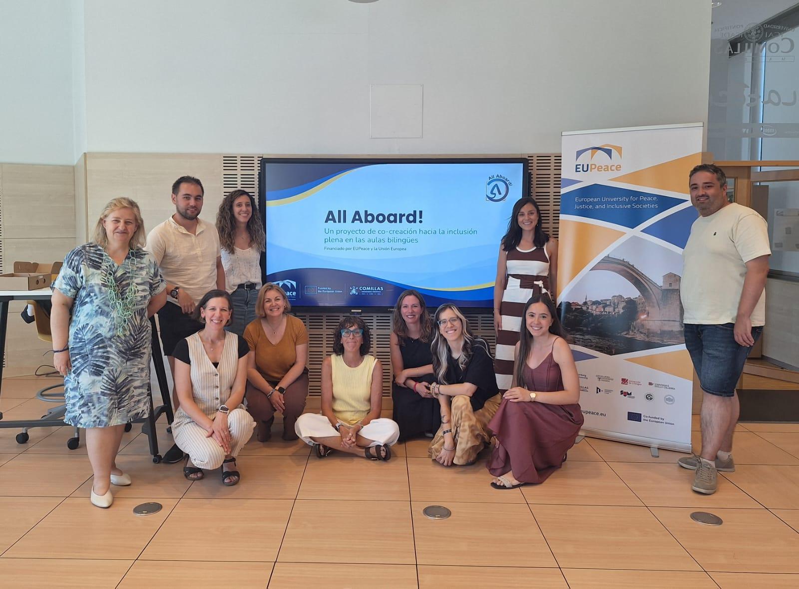 Un grupo de personas sonrientes posan frente a una pantalla con un mensaje sobre un proyecto llamado 'All Aboard'.