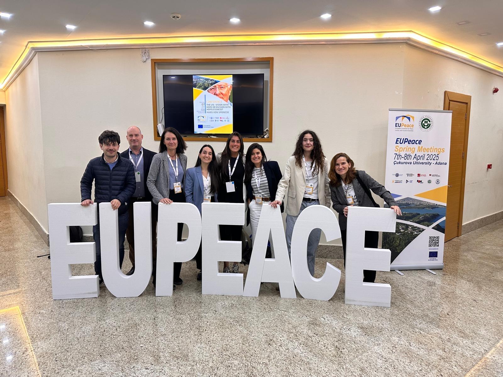Un grupo de personas posando junto a grandes letras que forman la palabra EUPEACE en un evento.