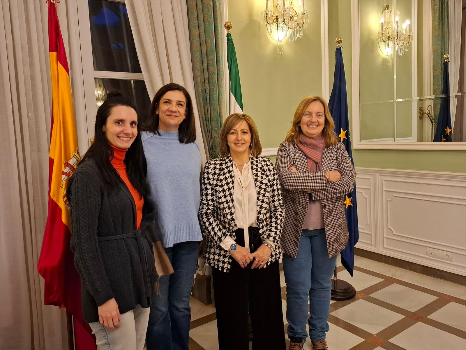 Cuatro mujeres sonriendo, de pie en una sala con banderas de España y la Unión Europea.